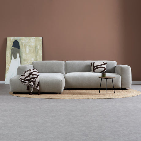 Lichtgrijze chaise longue bank met links chaise, sierkussen en bijzettafeltje.