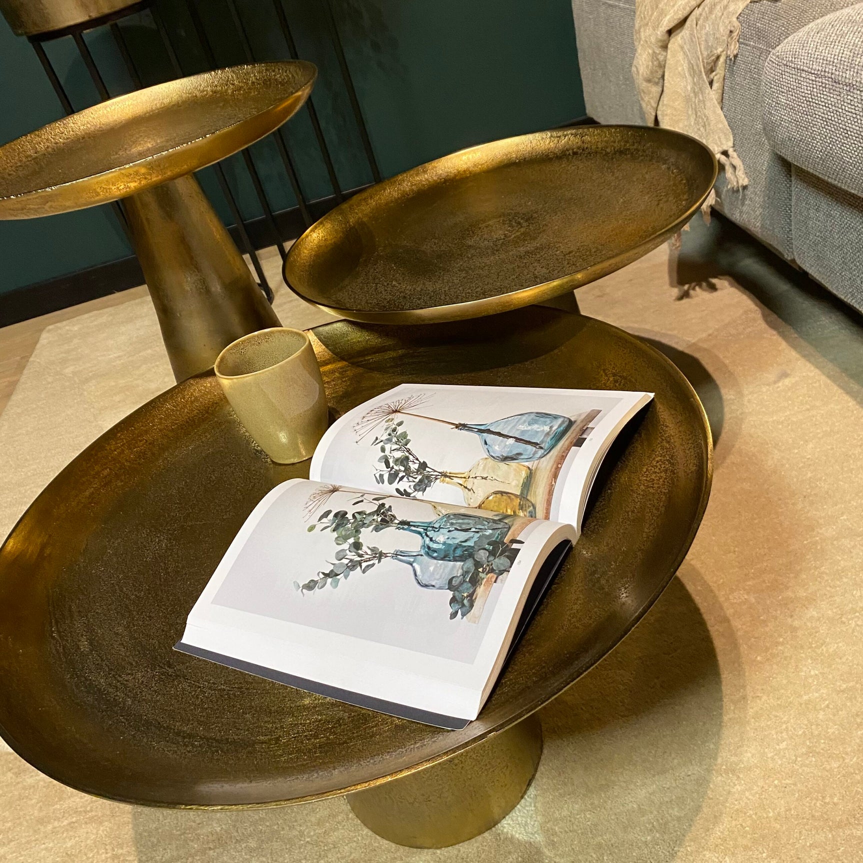 Goudkleurige salontafel met afgeronde rand, open tijdschrift en kopje erop