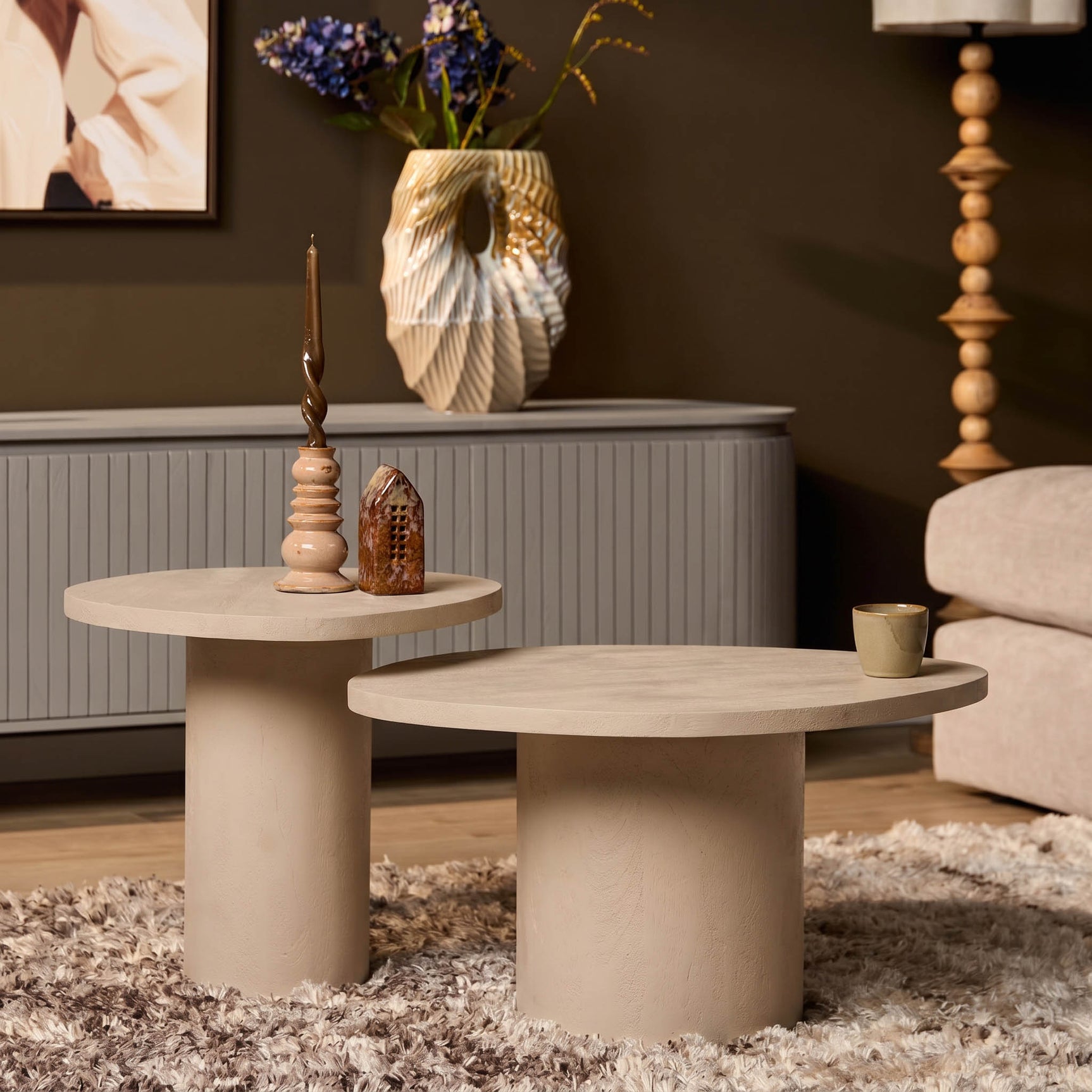 Twee ronde salontafels in zandkleur met glad blad en cilinderpoten, met kaars