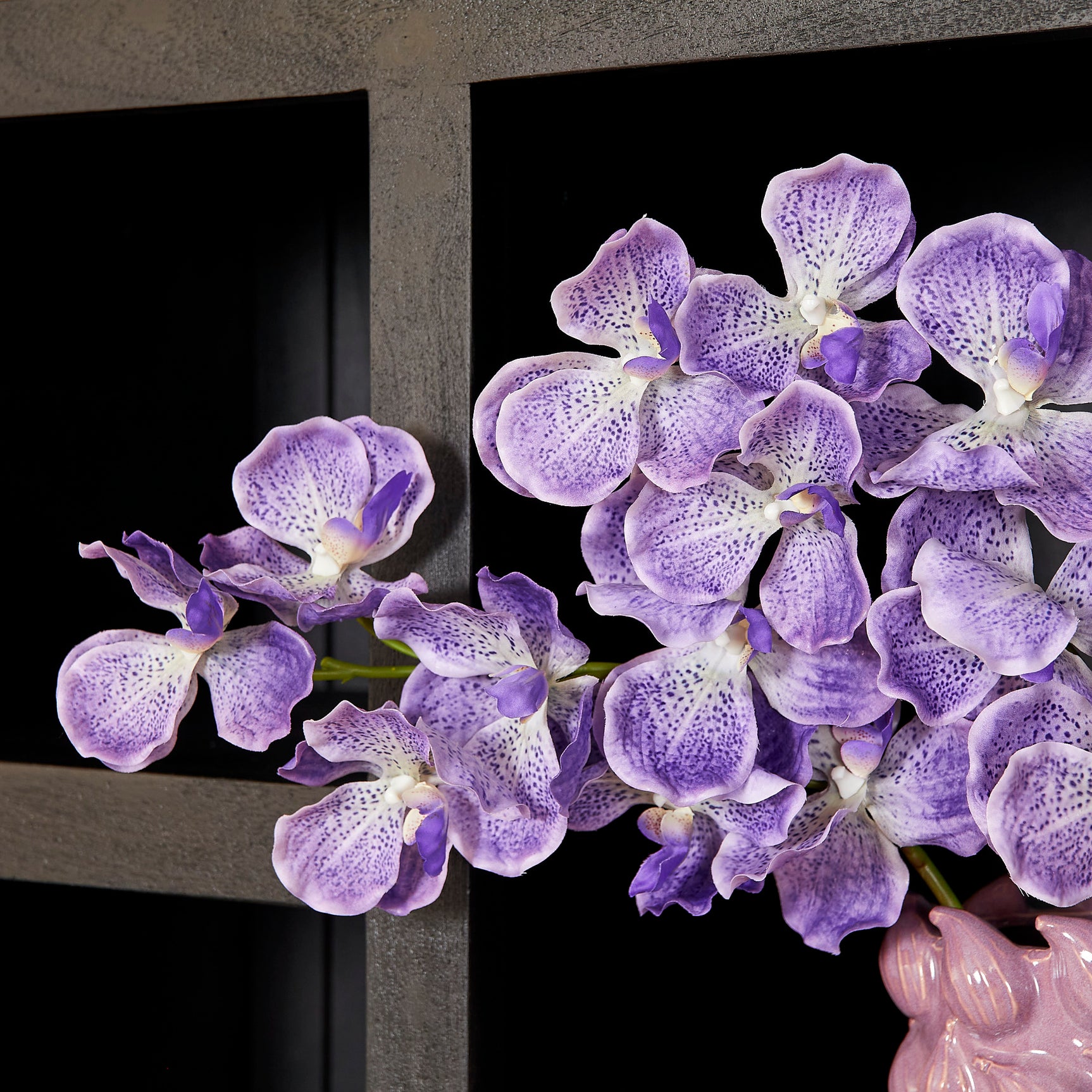 Paarse orchideeën in vaas op plank van zwarte boekenkast met open vak