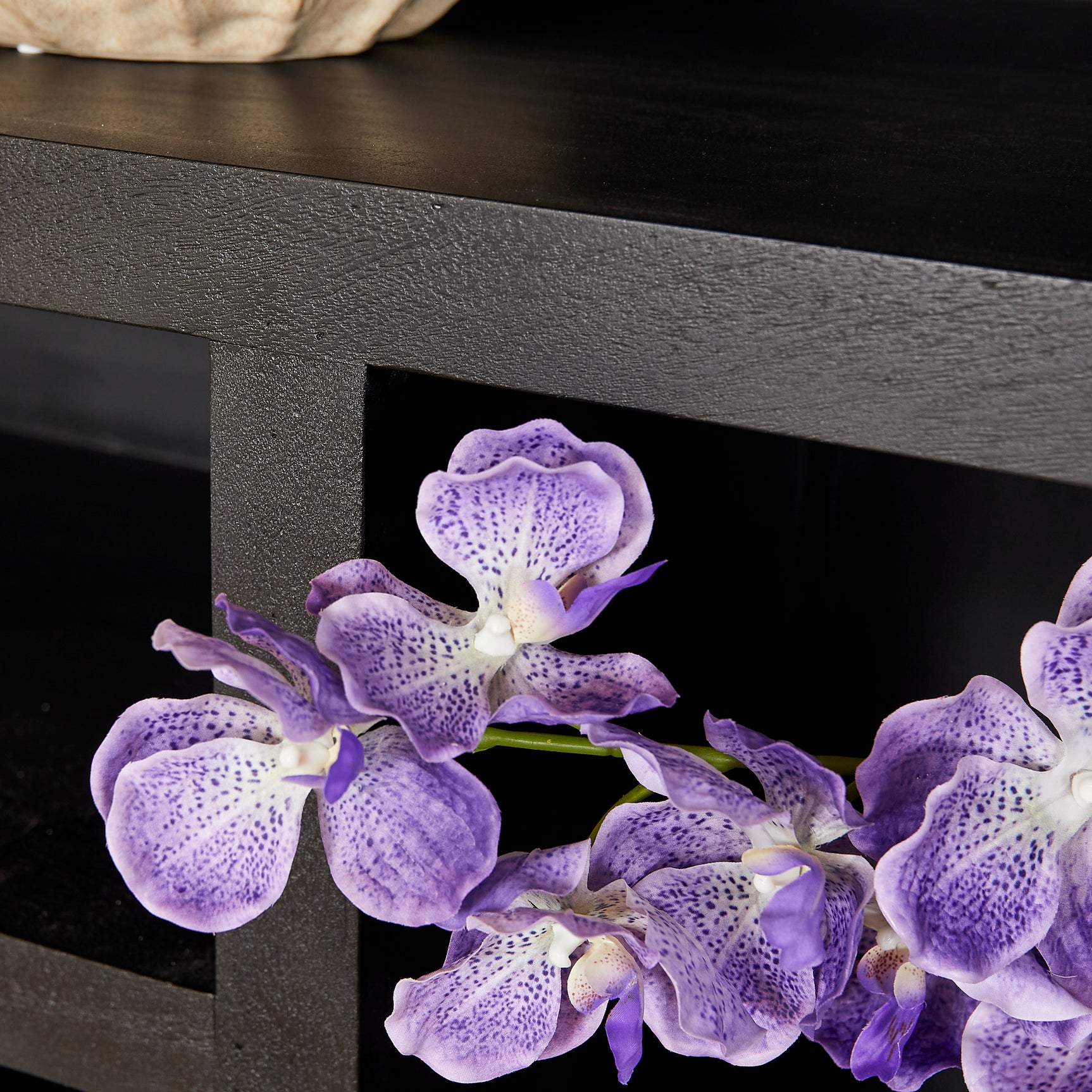 Zwarte vakkenkast met open vak en decoratieve orchidee op schap