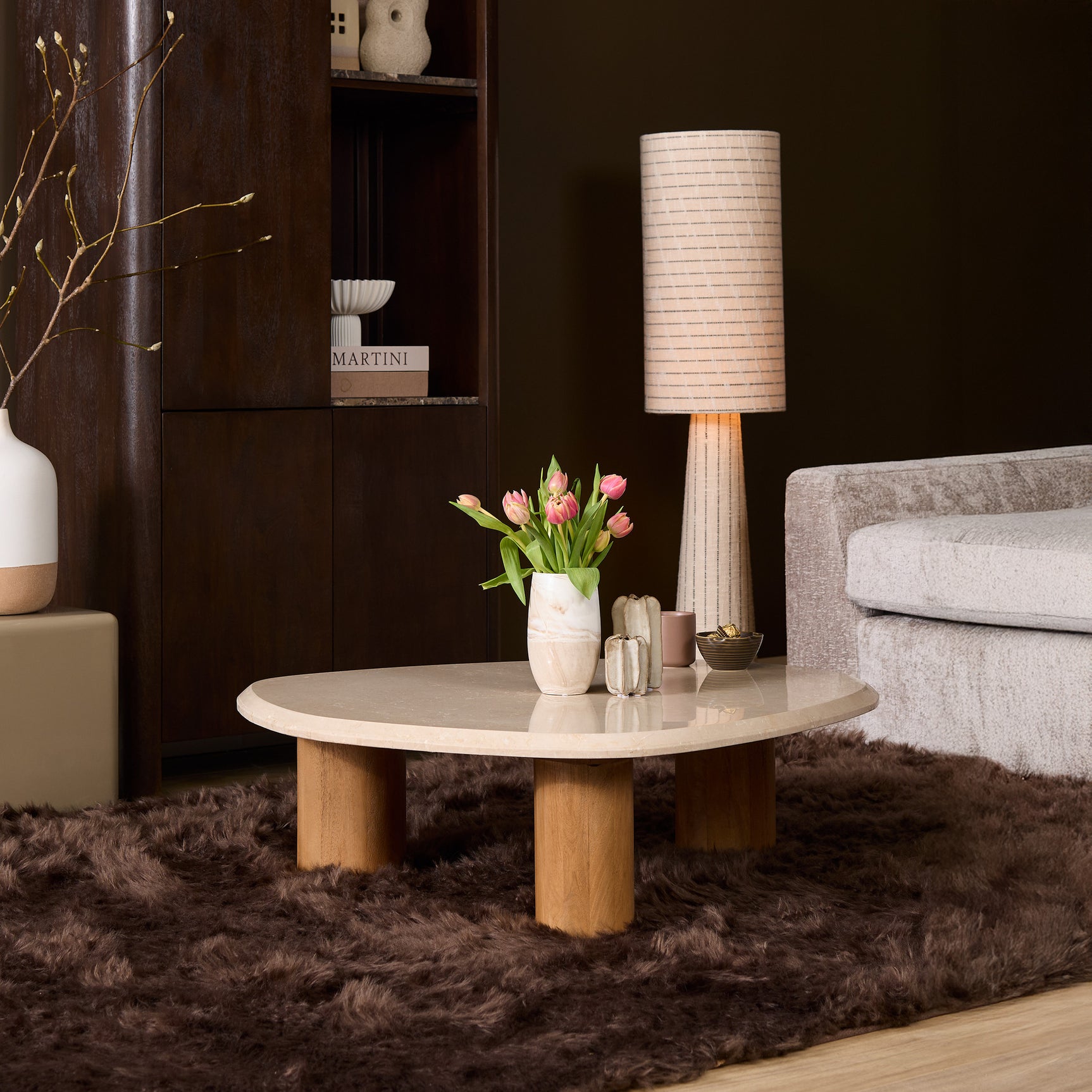 Ronde salontafel met licht marmeren blad en houten poot in woonkamer, met bloemenvaas