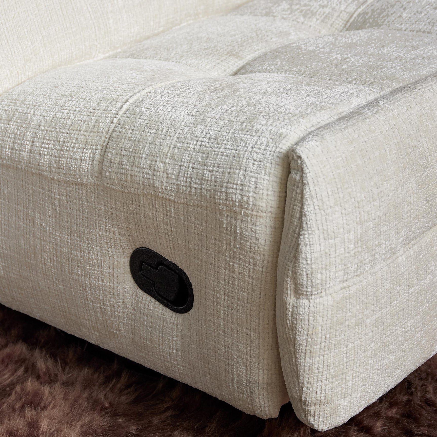 Gebroken witte fauteuilzitting met zwarte bedieningsknop en geweven stofstructuur.