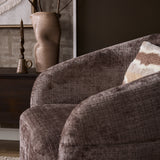 Fauteuil Yara met beige geweven stof en zijkant; decoratieve kussen ligt deels op de arm