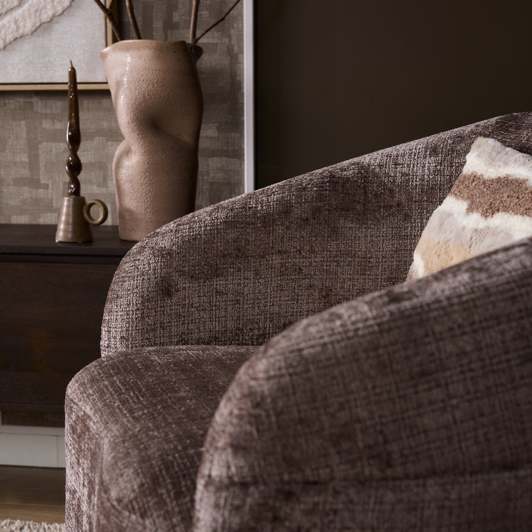 Fauteuil Yara met beige geweven stof en zijkant; decoratieve kussen ligt deels op de arm