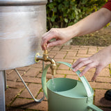 Zinken regenton met messing kraan en groene gieter op terras