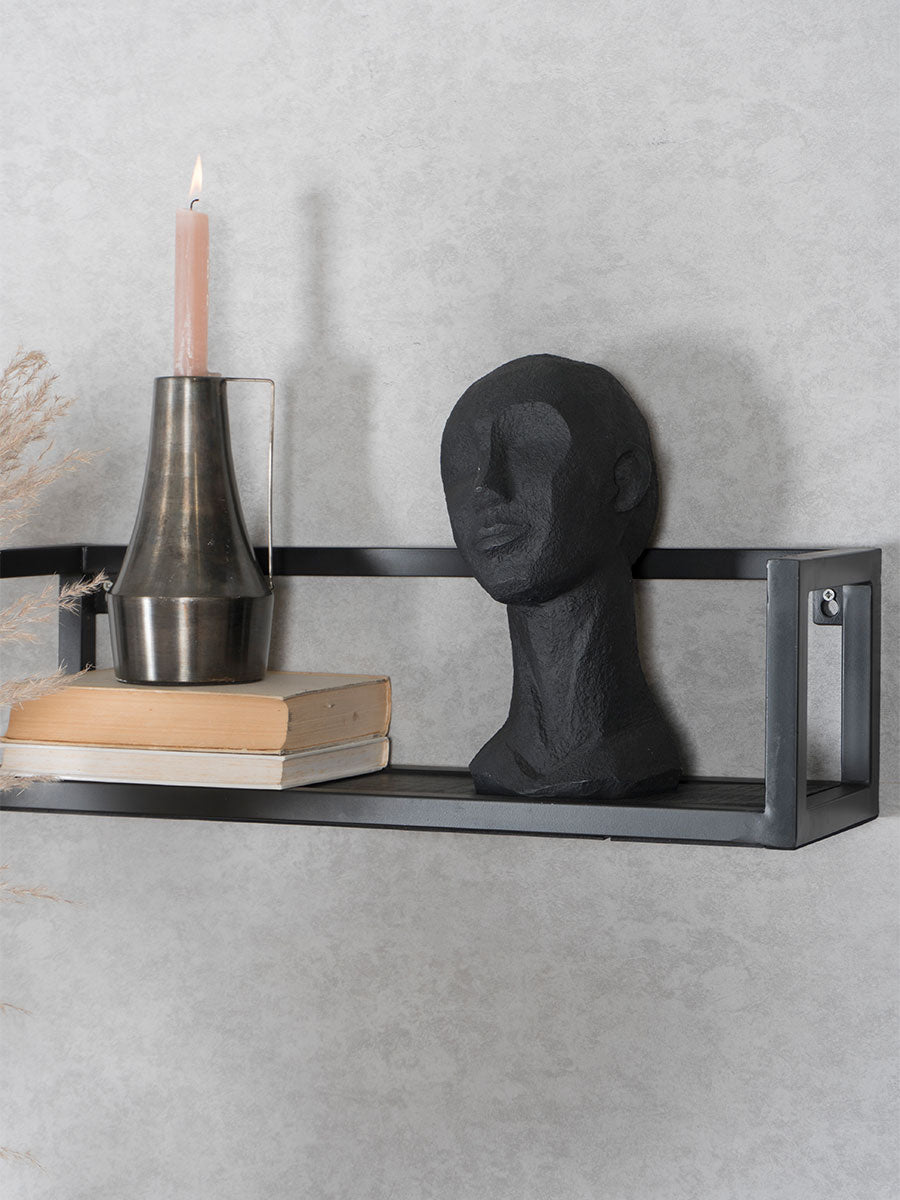 Zwarte metalen wandplank met houten plank en beugels, met kaars en hoed erop